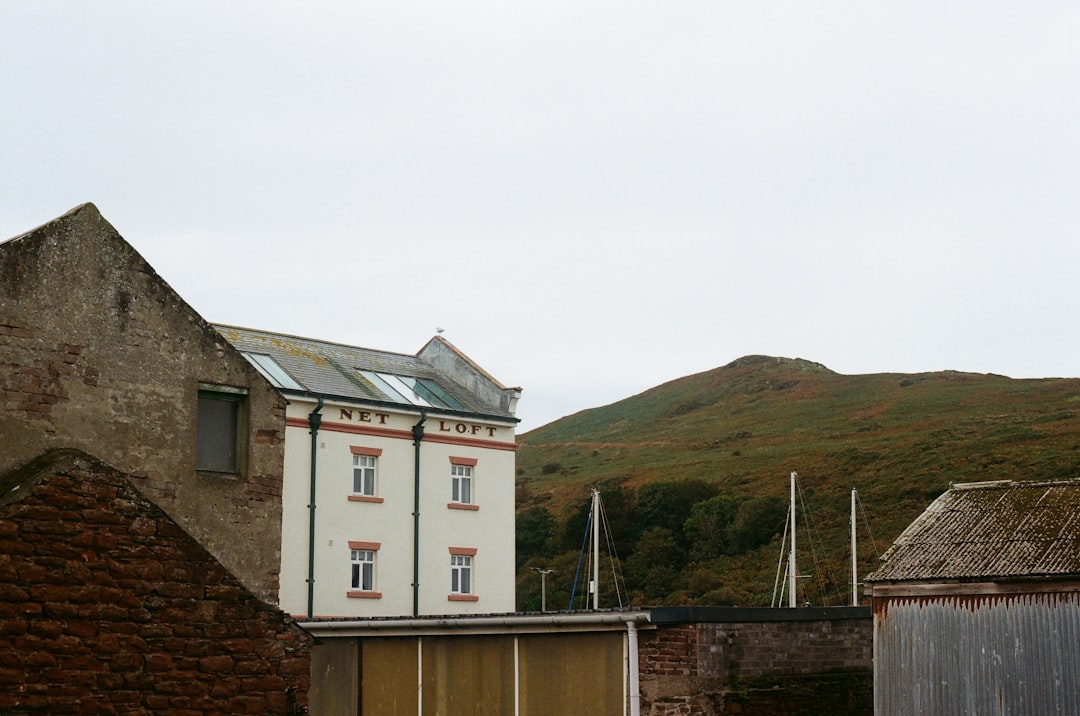 A white building with red trim stands out against a backdrop of rolling hills and cloudy skies.