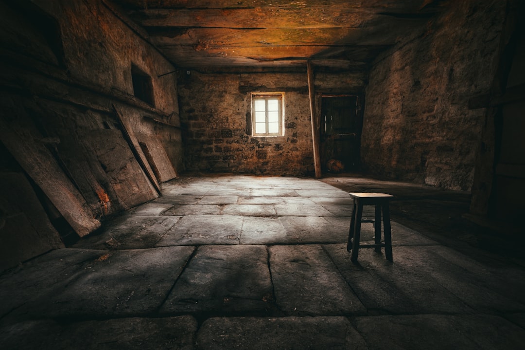A dimly lit room with a small window and a stool, exuding an eerie atmosphere.