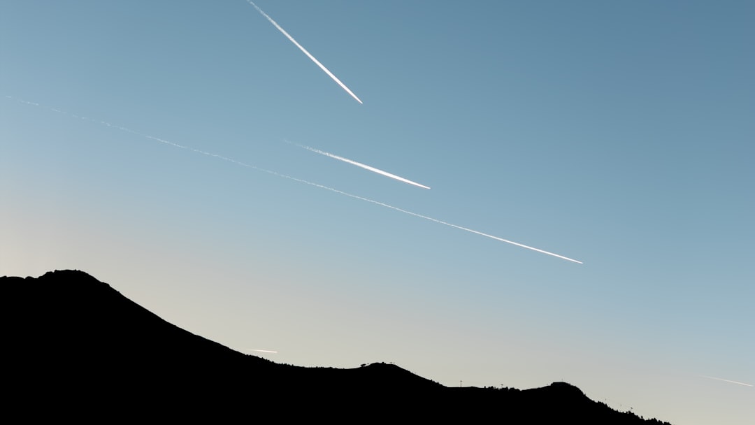 Five contrails streak across the sky above a mountain range.