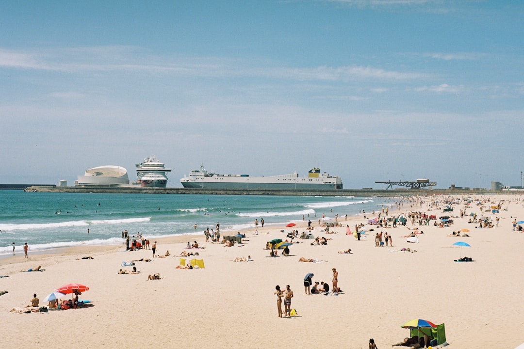 A bustling beach scene unfolds, with a vibrant array of sunbathers and beach umbrellas dotting the sand.