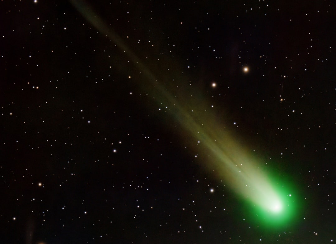 A bright green comet streaks through the dark night sky, its radiant tail illuminating the surrounding stars.