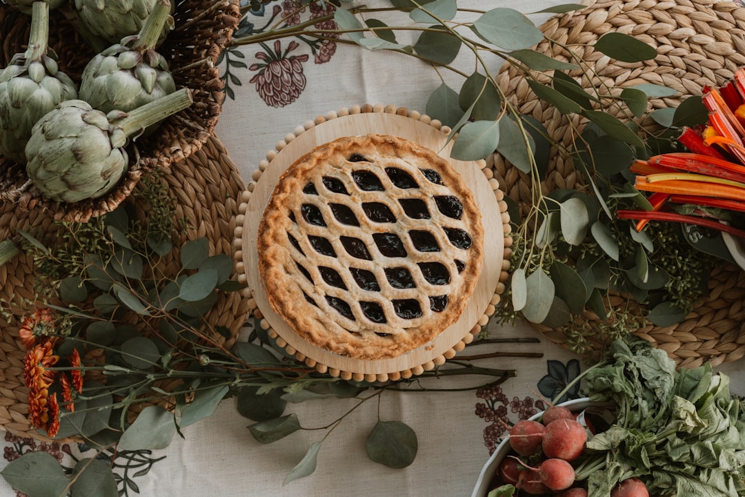 A lattice-topped pie takes center stage on a table, surrounded by an assortment of fresh produce and lush greenery.