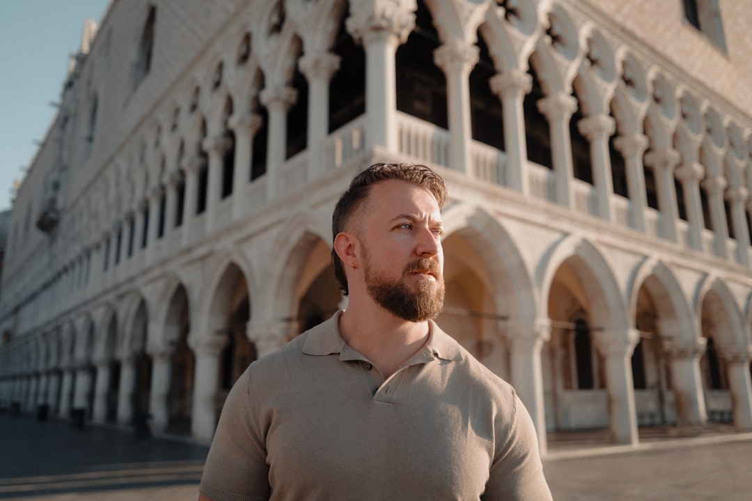 A man stands in front of a grand, ornate building with arches.