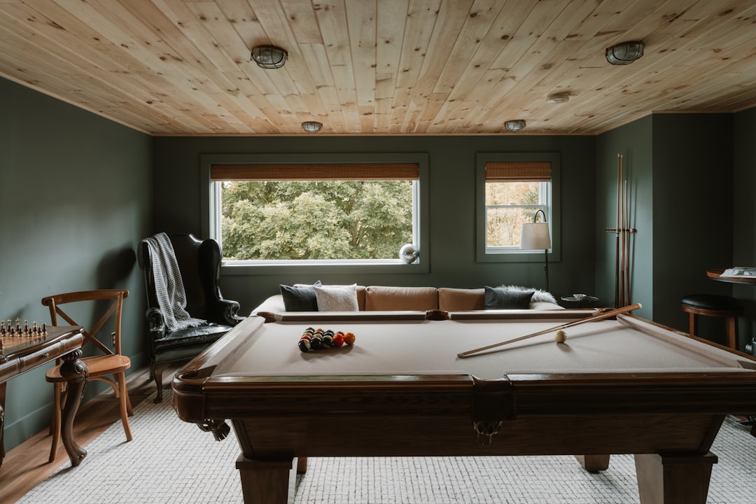 A cozy living room with a pool table, surrounded by a comfortable couch and natural light.