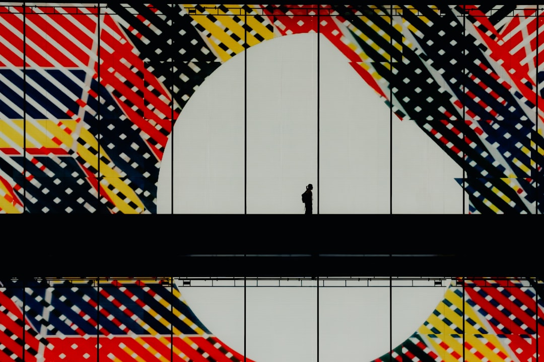 A person stands in front of a large white circle, surrounded by a vibrant mosaic of red, yellow, black, and white colors.
