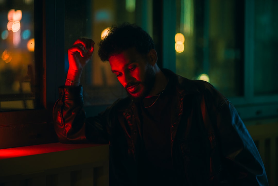 A man stands in a dimly lit room, illuminated by red and blue lights.