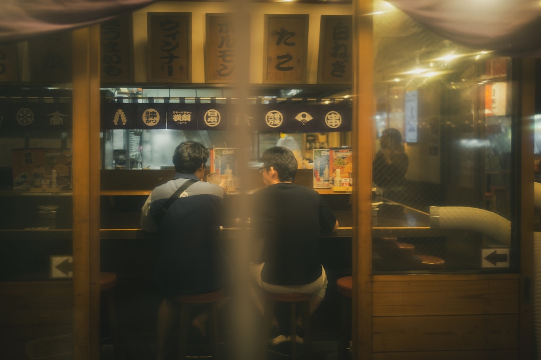 Two men sit at a counter, facing away from the camera, in a dimly lit restaurant.