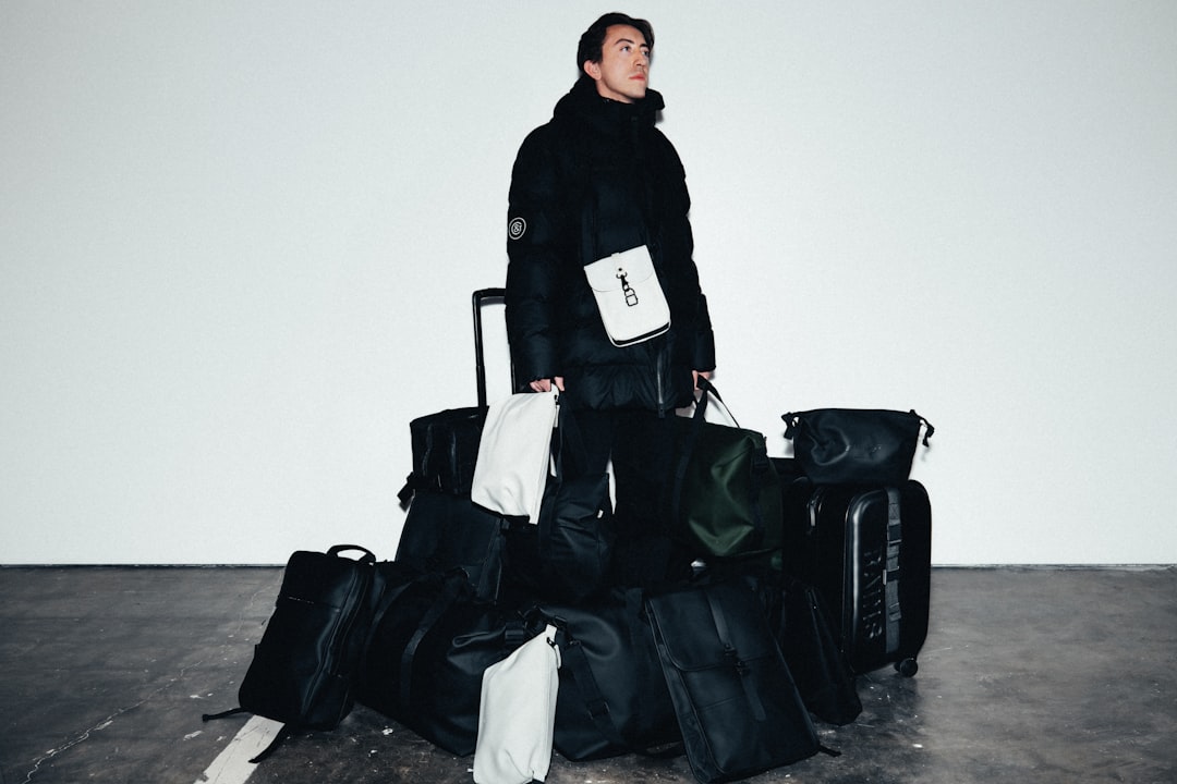 A man stands amidst a pile of black luggage, holding a white bag in his hand.