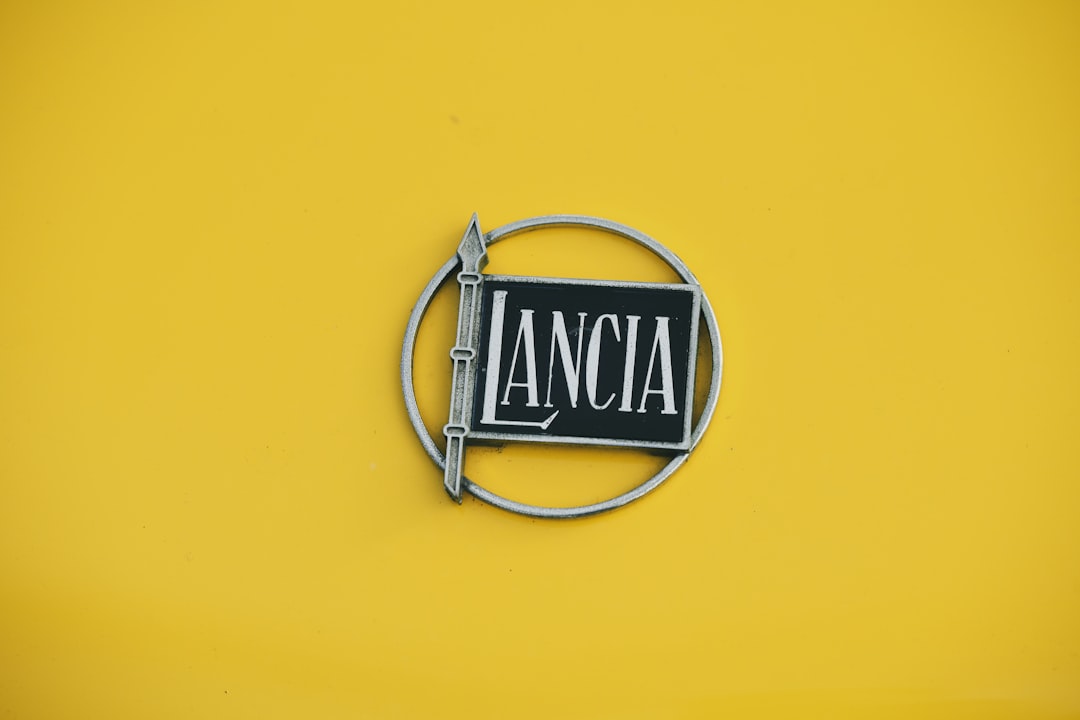 A silver Lancia logo is prominently displayed on a vibrant yellow background.