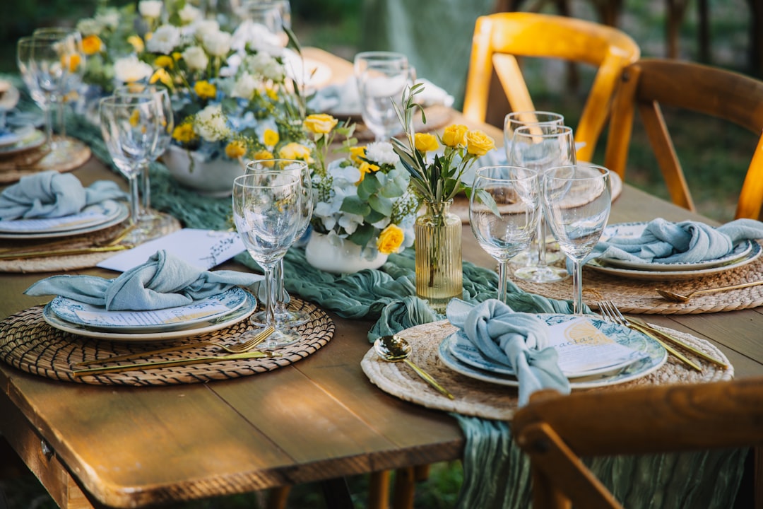 A wooden table set with plates, glasses, and a vase of yellow flowers.