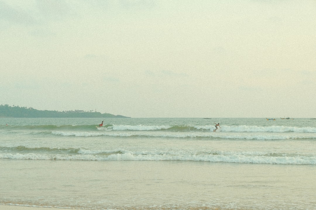 A lone surfer rides the waves, with a distant island and cloudy sky serving as a serene backdrop.