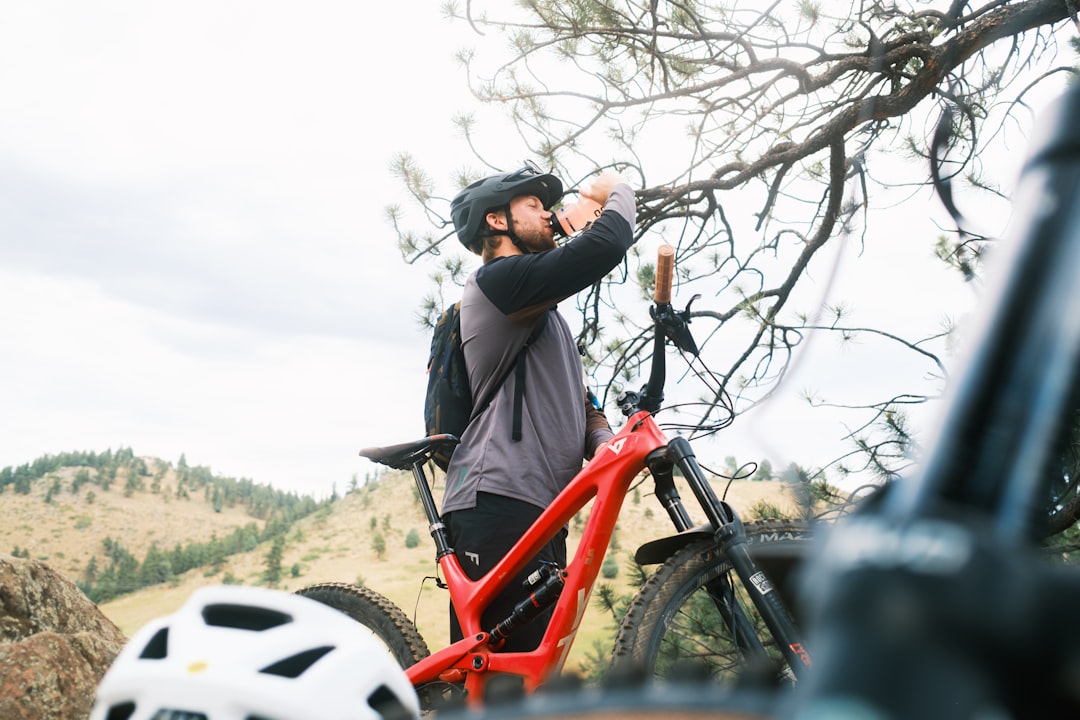 A man stands with a red bike, taking a break to drink from a bottle.