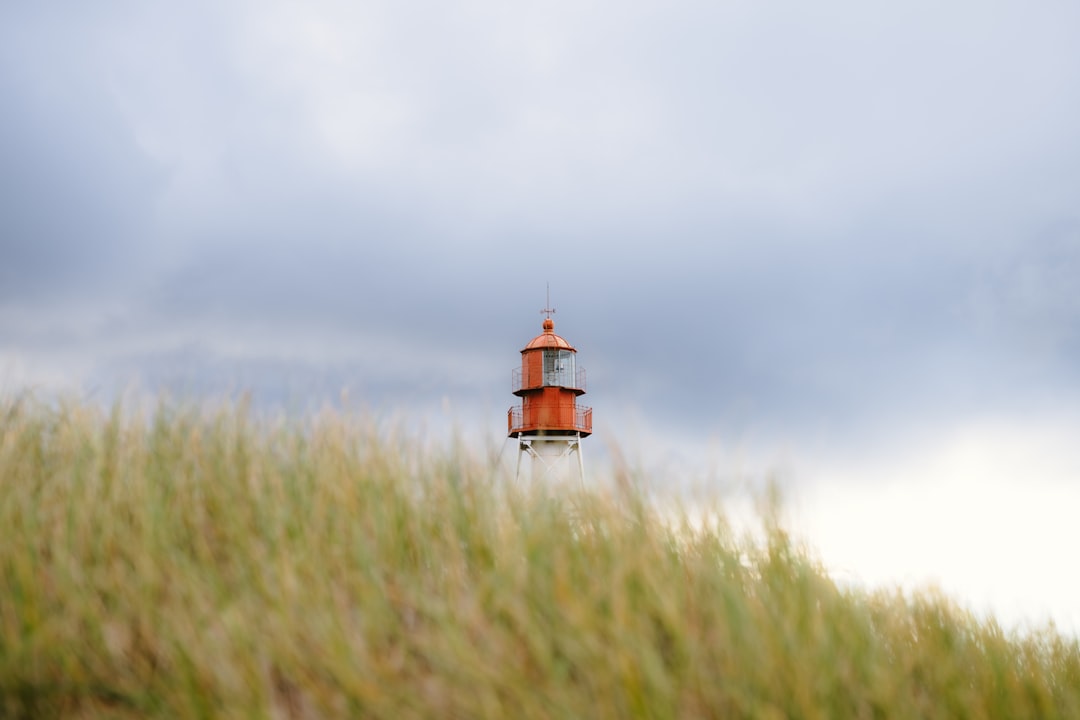 A vibrant orange lighthouse stands tall against a backdrop of stormy grey clouds.