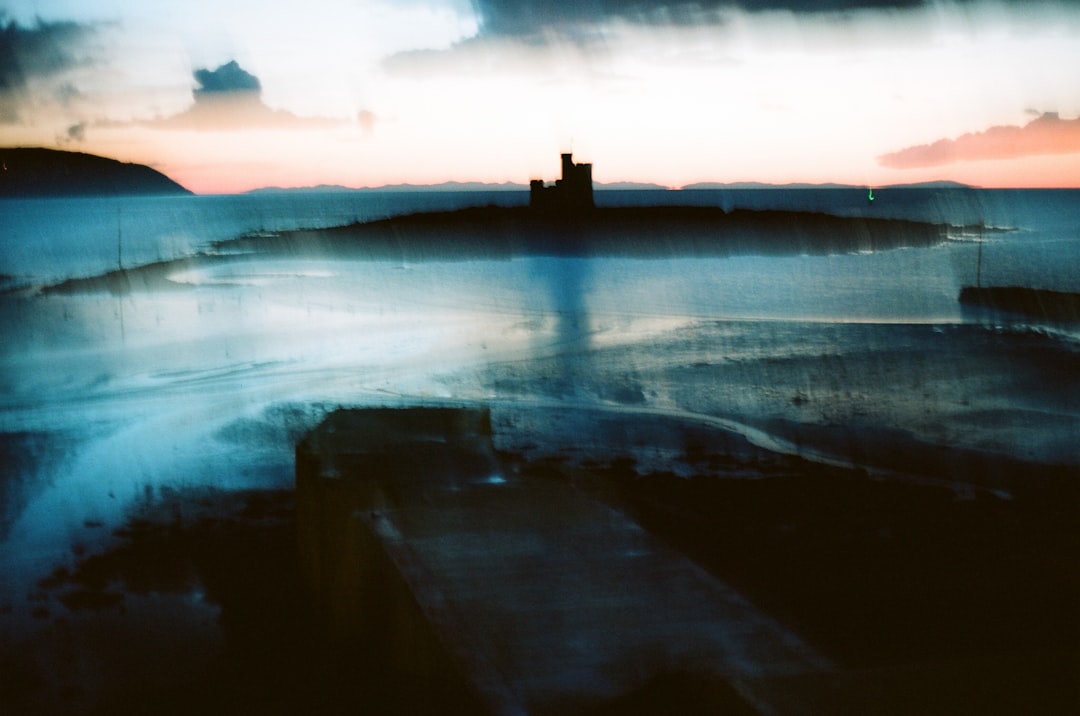 A castle stands tall on a distant island, surrounded by a vast body of water under a dramatic sky.