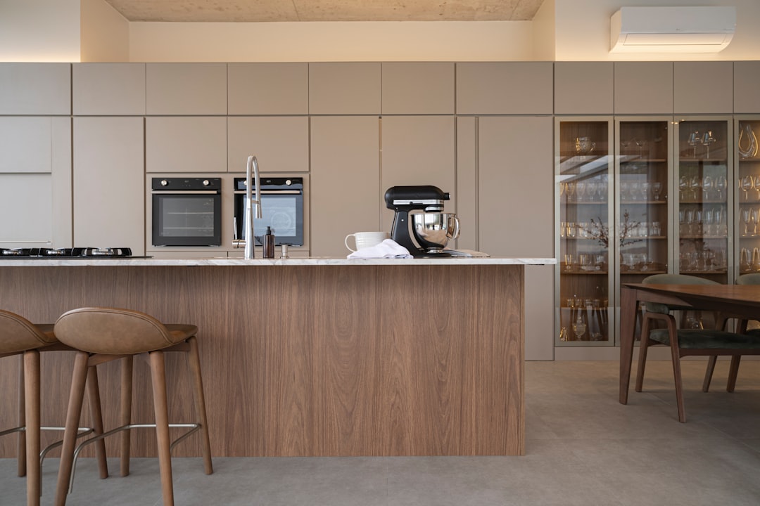 A sleek kitchen features a central island, complete with a sink and stools, surrounded by a range of appliances and a stylish dining area.