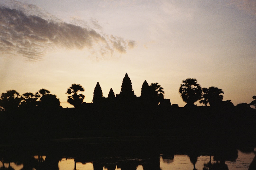 A majestic silhouette of a temple rises against a vibrant sky, surrounded by lush palm trees and a serene body of water.