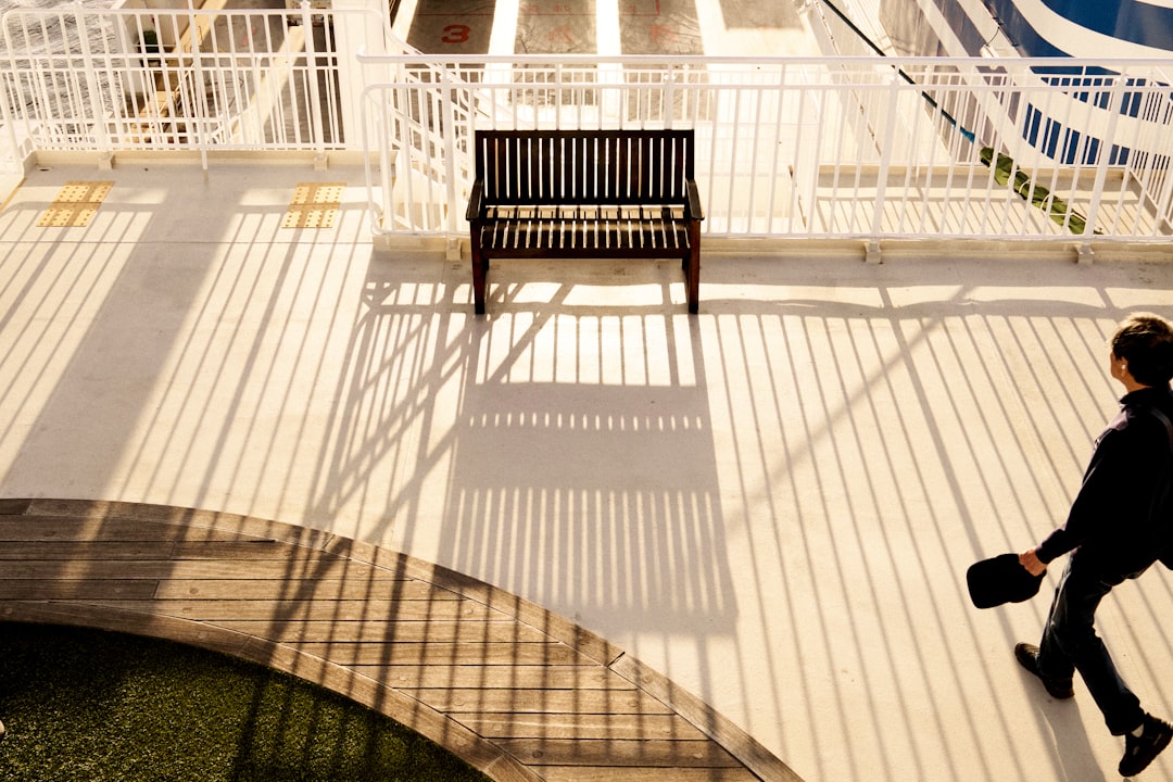 A man walks past a bench in a courtyard, surrounded by shadows cast by white railings.