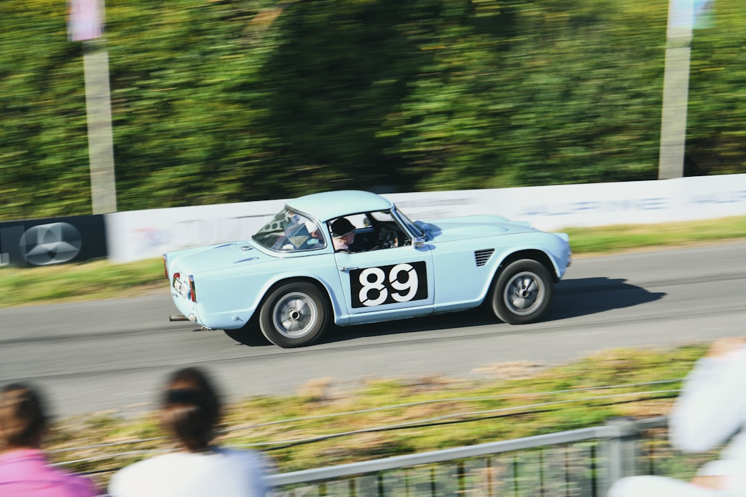 A vintage blue car with the number 89 on the door speeds down a road.