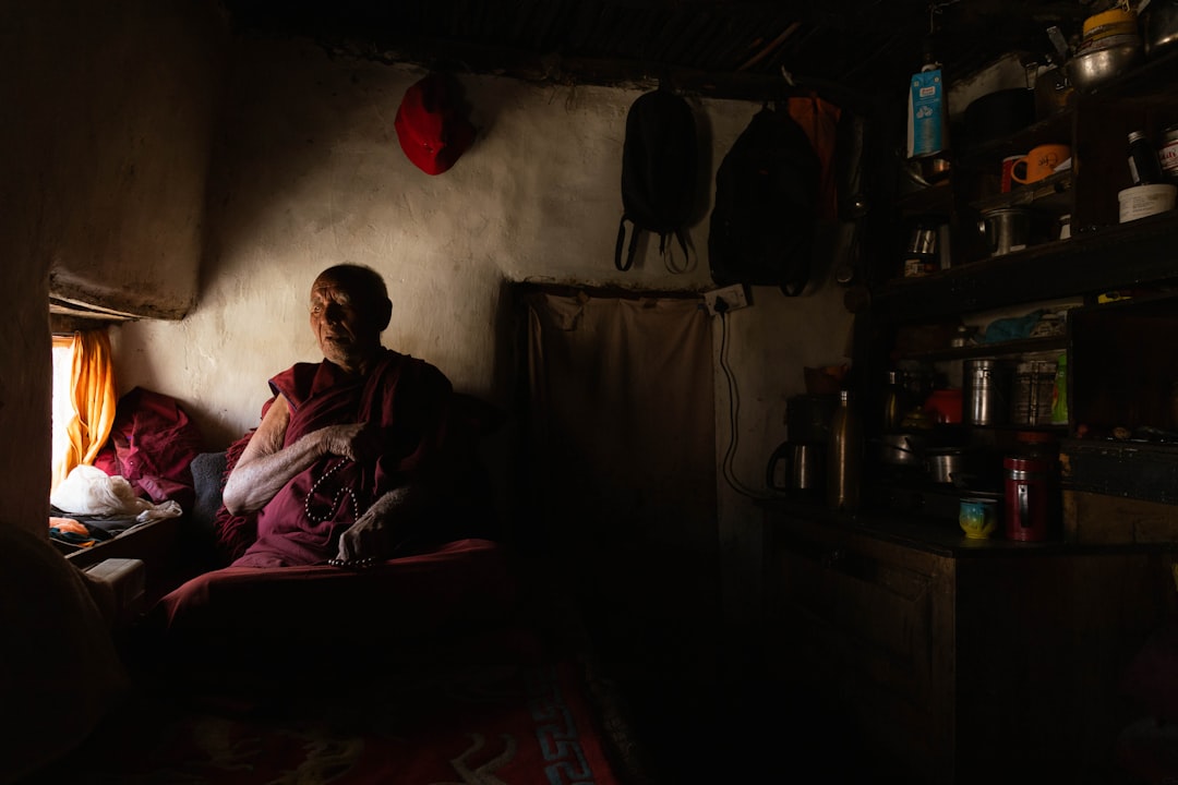 A Buddhist monk sits in a dimly lit room, illuminated by sunlight streaming through the window.