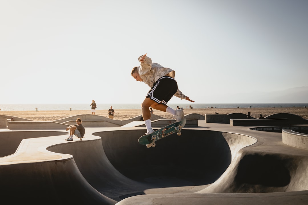 A skateboarder performs a trick on a concrete ramp, surrounded by a beach and ocean in the background.