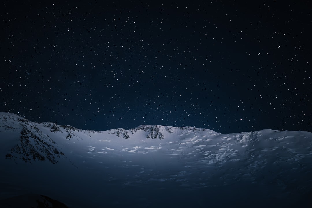 Snow-capped mountains stretch across a starry night sky.
