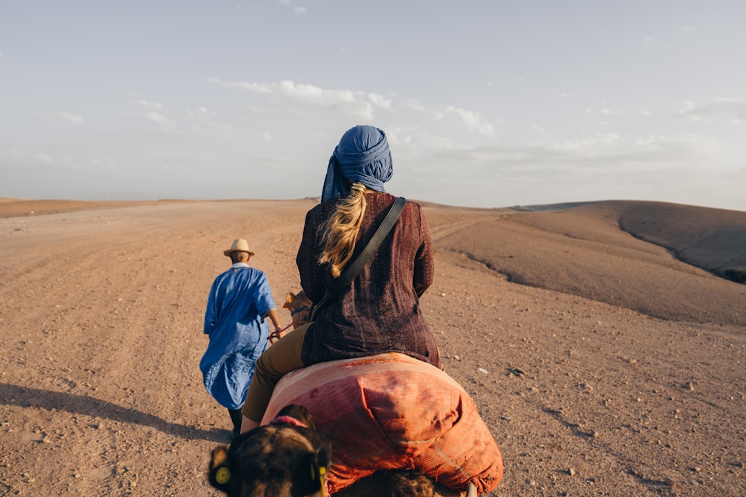 A woman rides a camel across a vast, arid landscape.