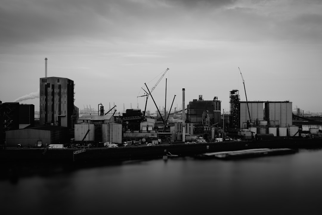 A large industrial facility is situated along the waterfront, with a prominent smokestack emitting smoke.