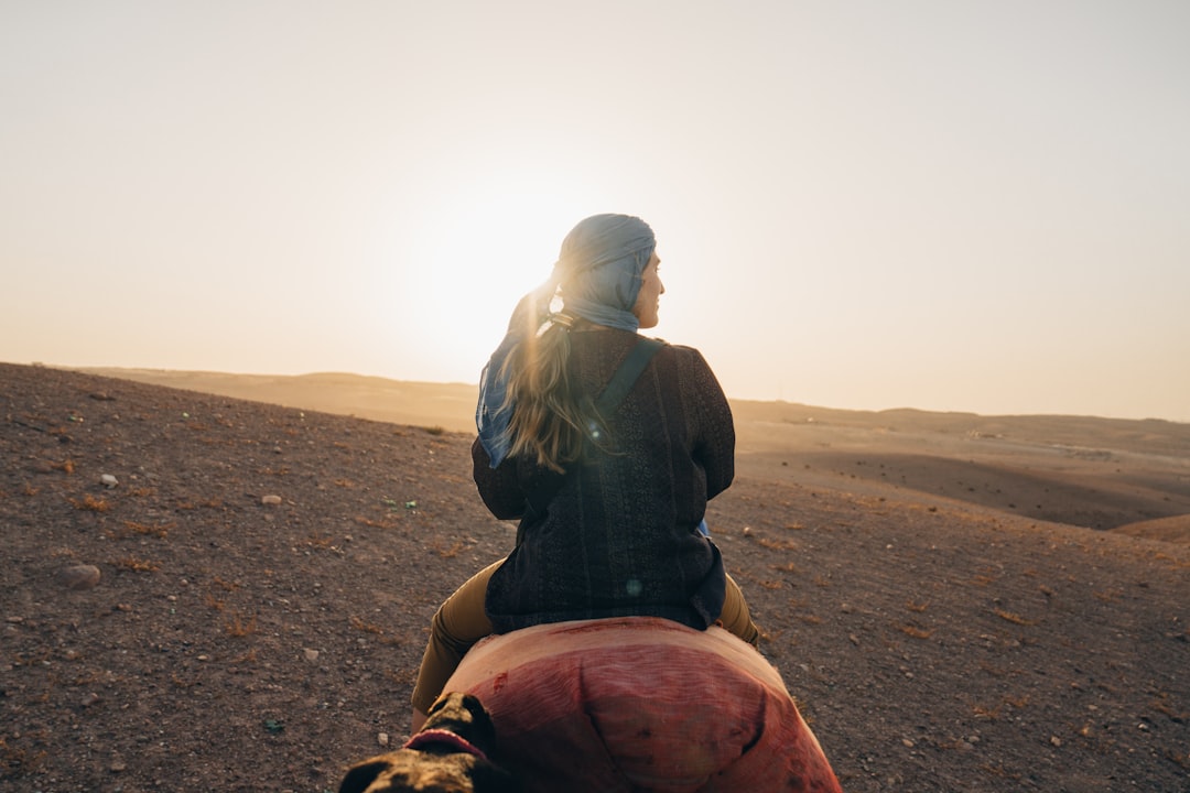 A woman sits on a camel's back, gazing out at the vast desert landscape.
