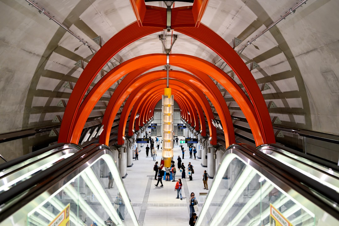 A spacious underground area with a striking red archway structure, surrounded by people and escalators.