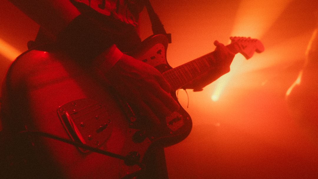 A musician's hands grasp a guitar, surrounded by a vibrant red and orange glow.