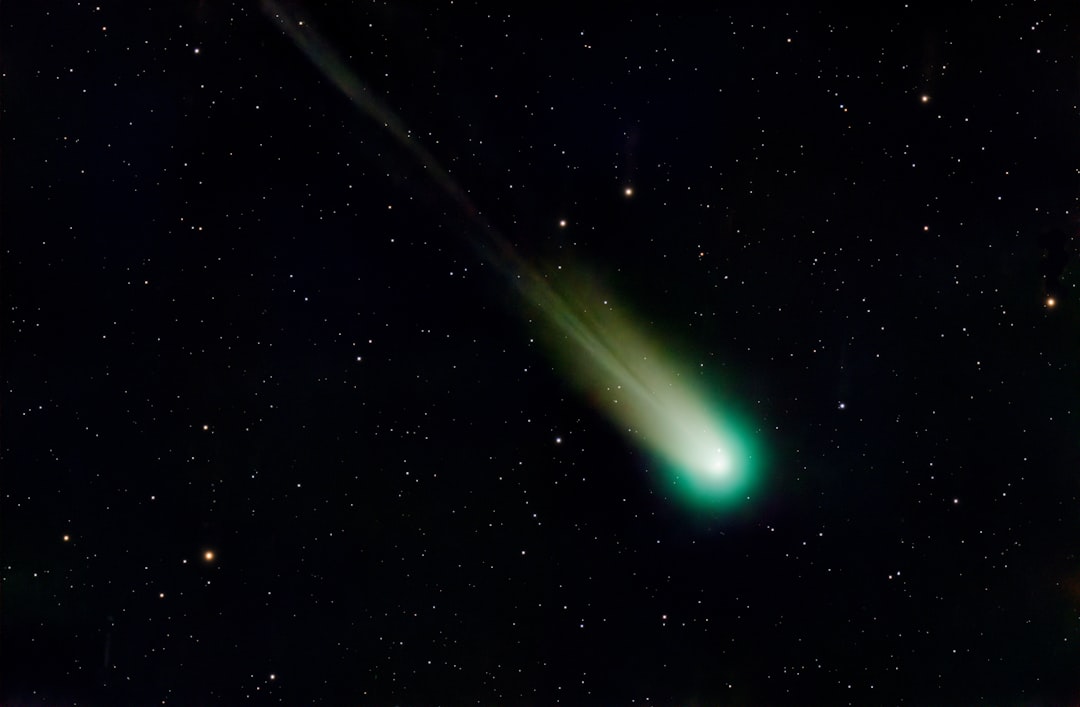 A comet streaks through the night sky, its green tail and bright nucleus shining brightly against a backdrop of twinkling stars.