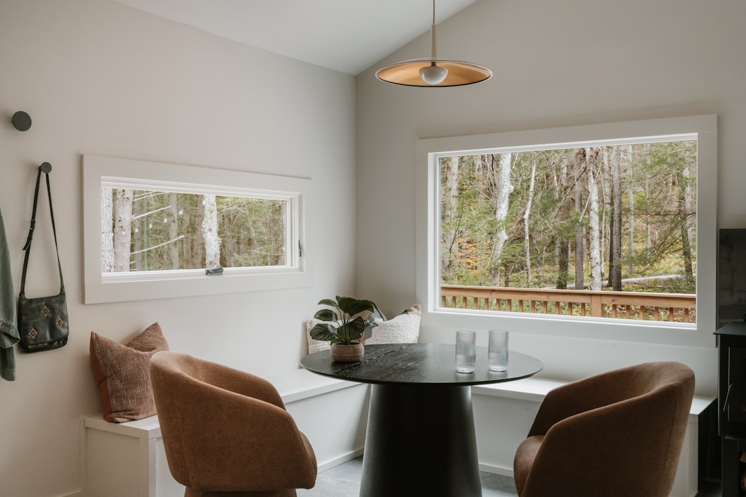 A cozy dining area with a view of a forest through a large window, featuring a small table and chairs.