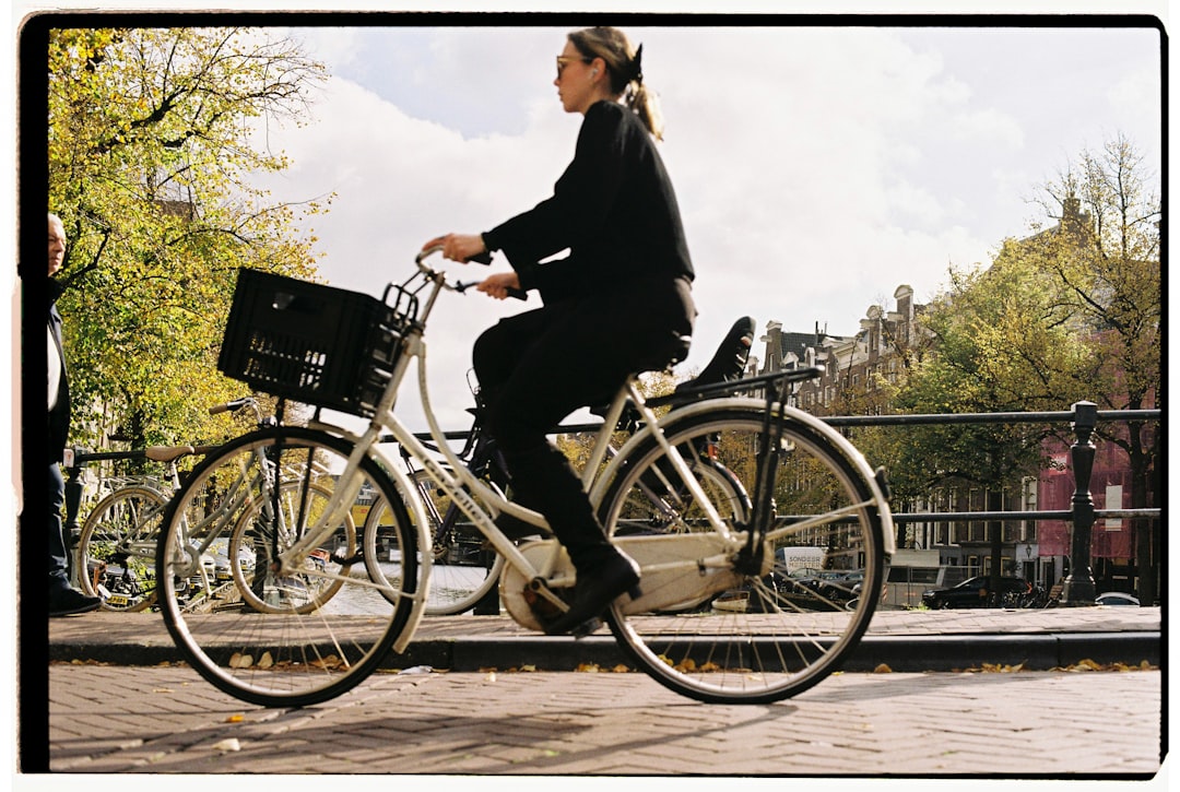 A woman rides a white bicycle with a black basket on the bridge.