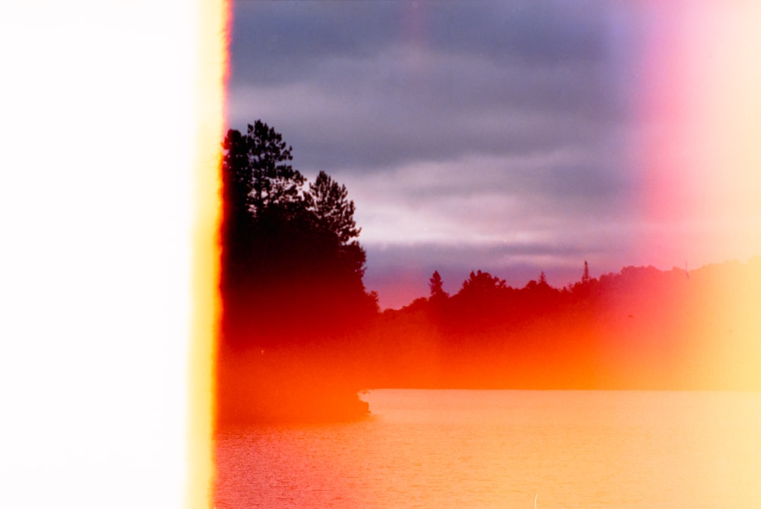 A lake glimmers under a vibrant sky, with trees silhouetted against a kaleidoscope of colors.