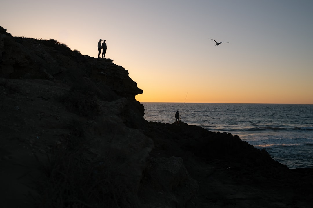 Two figures stand atop a rocky cliff, silhouetted against a vibrant sunset.