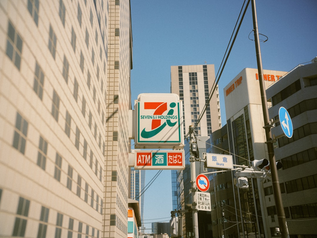 A sign stands between two buildings, featuring a green and orange logo with the words "Seven & I Holdings" in green.