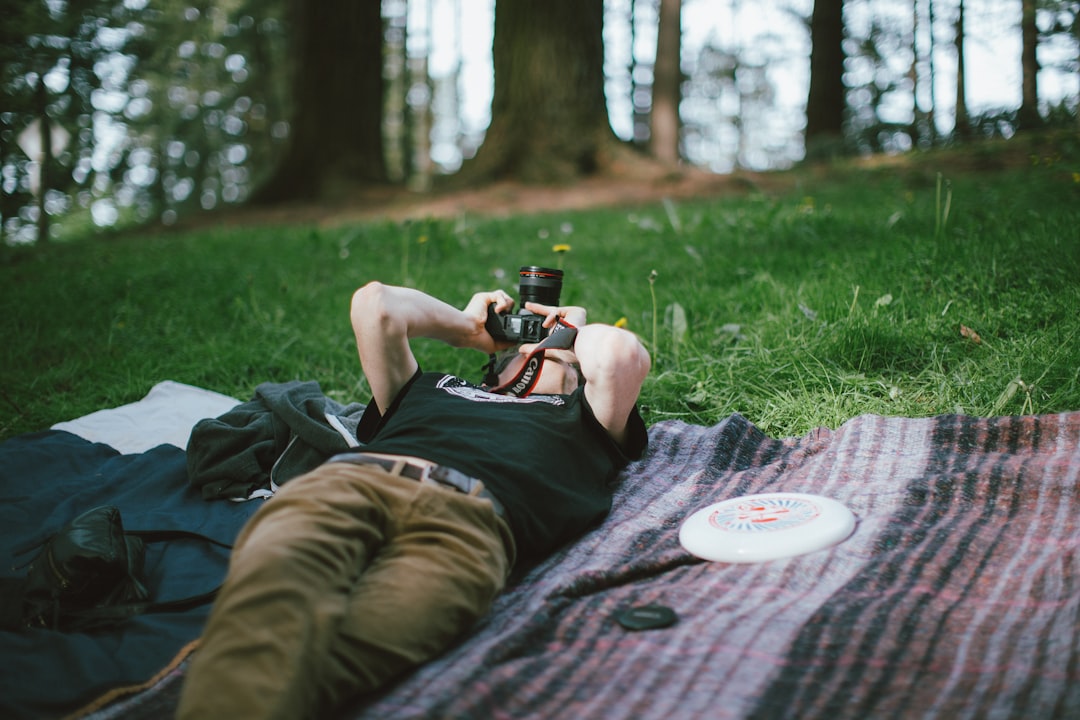 A man lies on a blanket in the grass, capturing a moment with his camera.