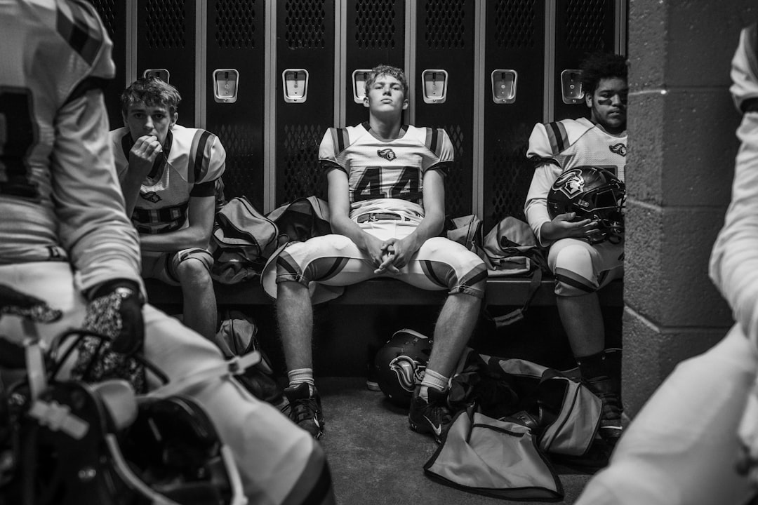 A football player sits in a locker room, surrounded by teammates.