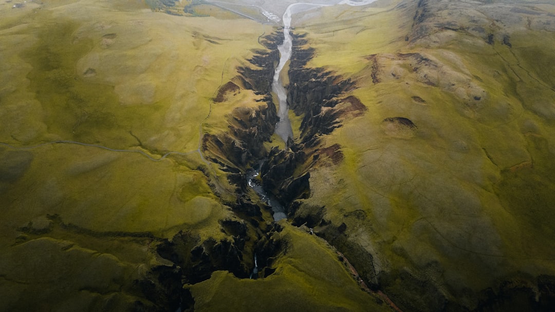 A narrow stream carves through a valley, surrounded by lush green hills.